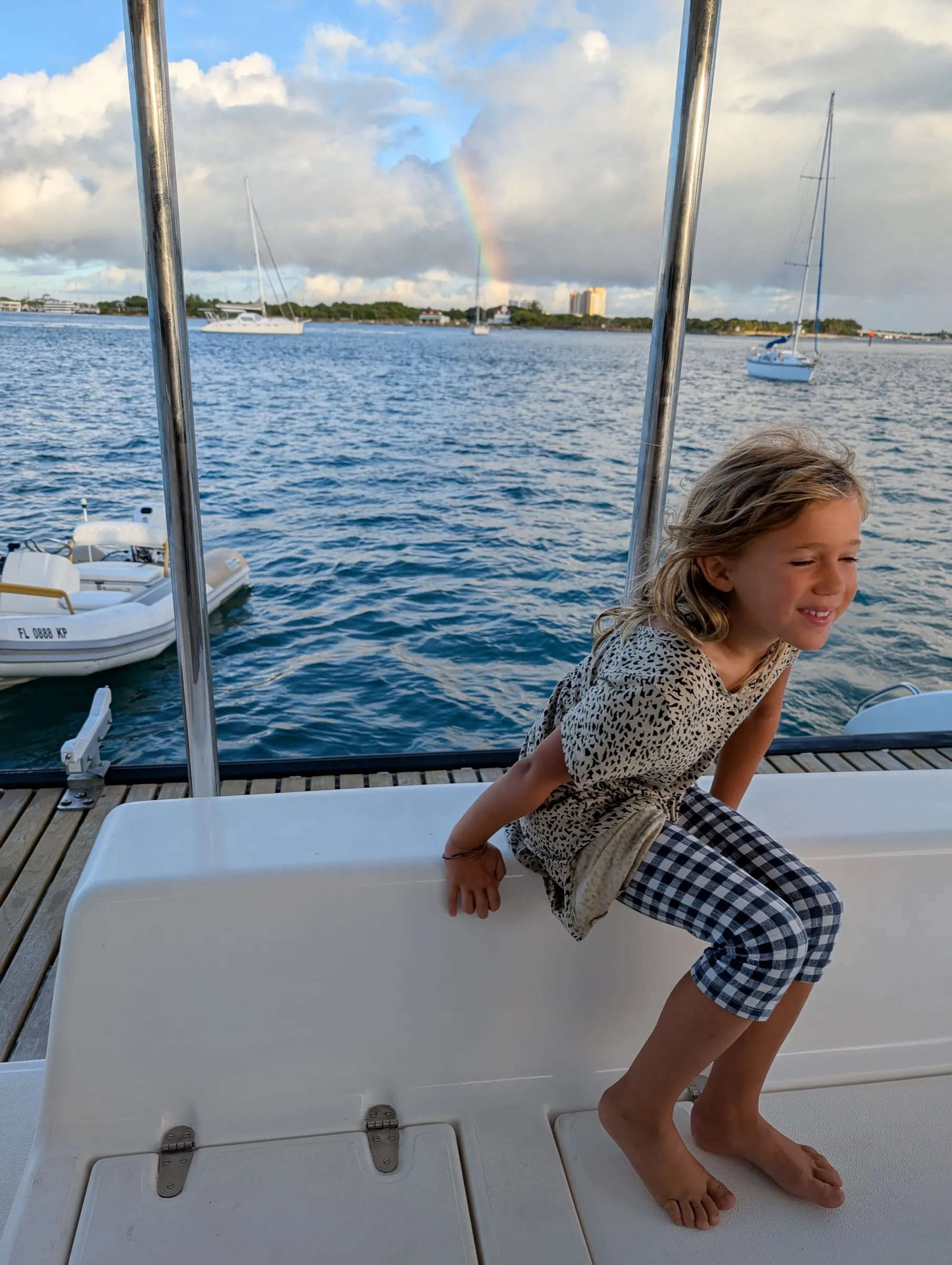 Young girl on the deck of the Voyage 500 catamaran with a vibrant rainbow arcing across the sky behind her